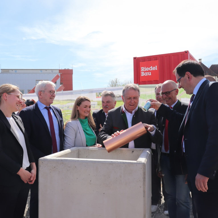 Grundsteinlegung in Kutzenberg: Gesundheitsministerin Judith Gerlach (3.v.li.), Staatssekretär Martin Schöffel (re.), Bezirkstagspräsident Henry Schramm (3.v.re.) und weitere Ehrengäste füllen die Zeitkapsel.